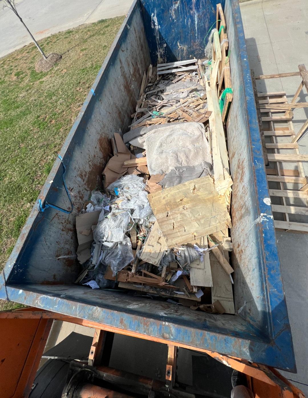 Dumpster overflowing with trash and pallets before compaction